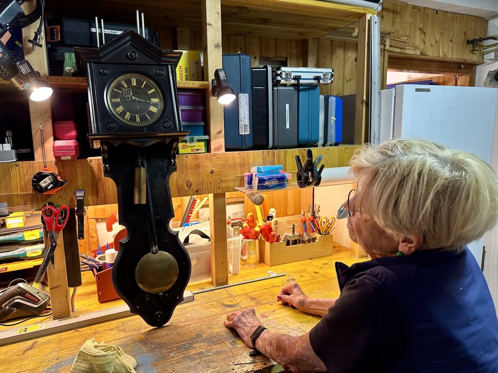 Alte Uhr in einer Werkstatt. Eine Frau betrachtet die Uhr.