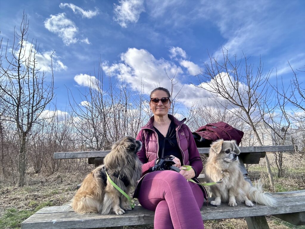 Eine Frau sitzt mit 2 Hunden auf einer Bank im Freien.